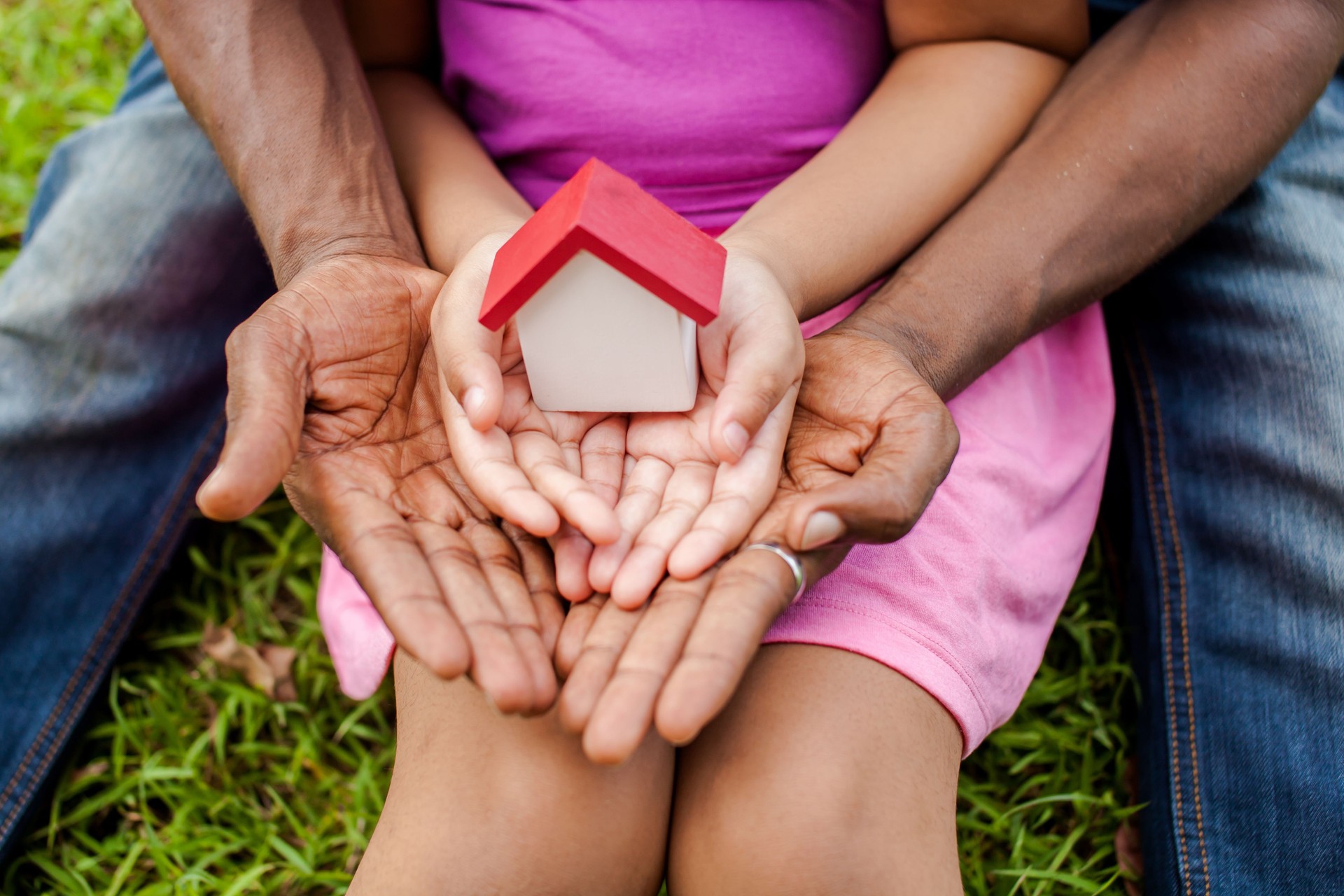Mãos da família juntas segurando casa em parque verde
